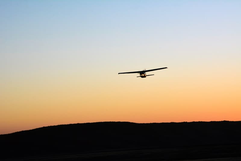 A lone small single-engine plane flies in the clear evening sky. Only the outline of the plane is visible. Front view